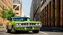 Зеленый Plymouth Barracuda блуждает в городских застройках